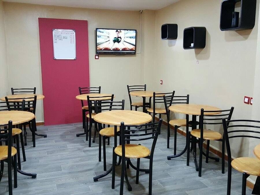 Una habitación con varias mesas redondas y sillas, una puerta roja, un tablón de anuncios y un televisor en la pared.