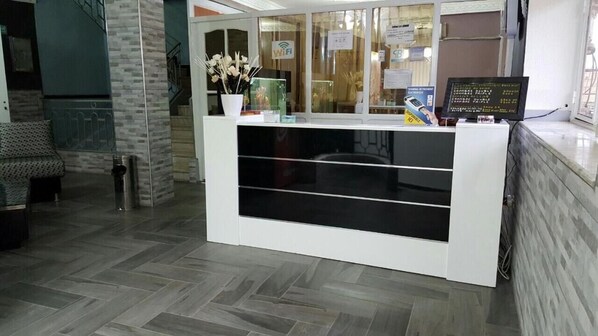 A reception desk with a modern design, a vase with flowers, and a monitor displaying information.