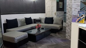 A modern hotel lobby with a sectional sofa, a glass coffee table, and a reception desk with a flag. - Hôtel La Brise (Ain El Turk)