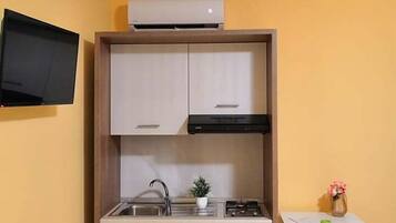 A compact kitchen with a built-in stove, sink, and cabinets, a small table with a chair, and a flat-screen TV mounted on the wall.