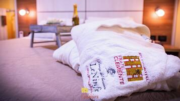 A hotel room with a neatly made bed, a bedside table with a bottle, and a chair. The room has a modern design with a wooden headboard and wall-mounted lights.