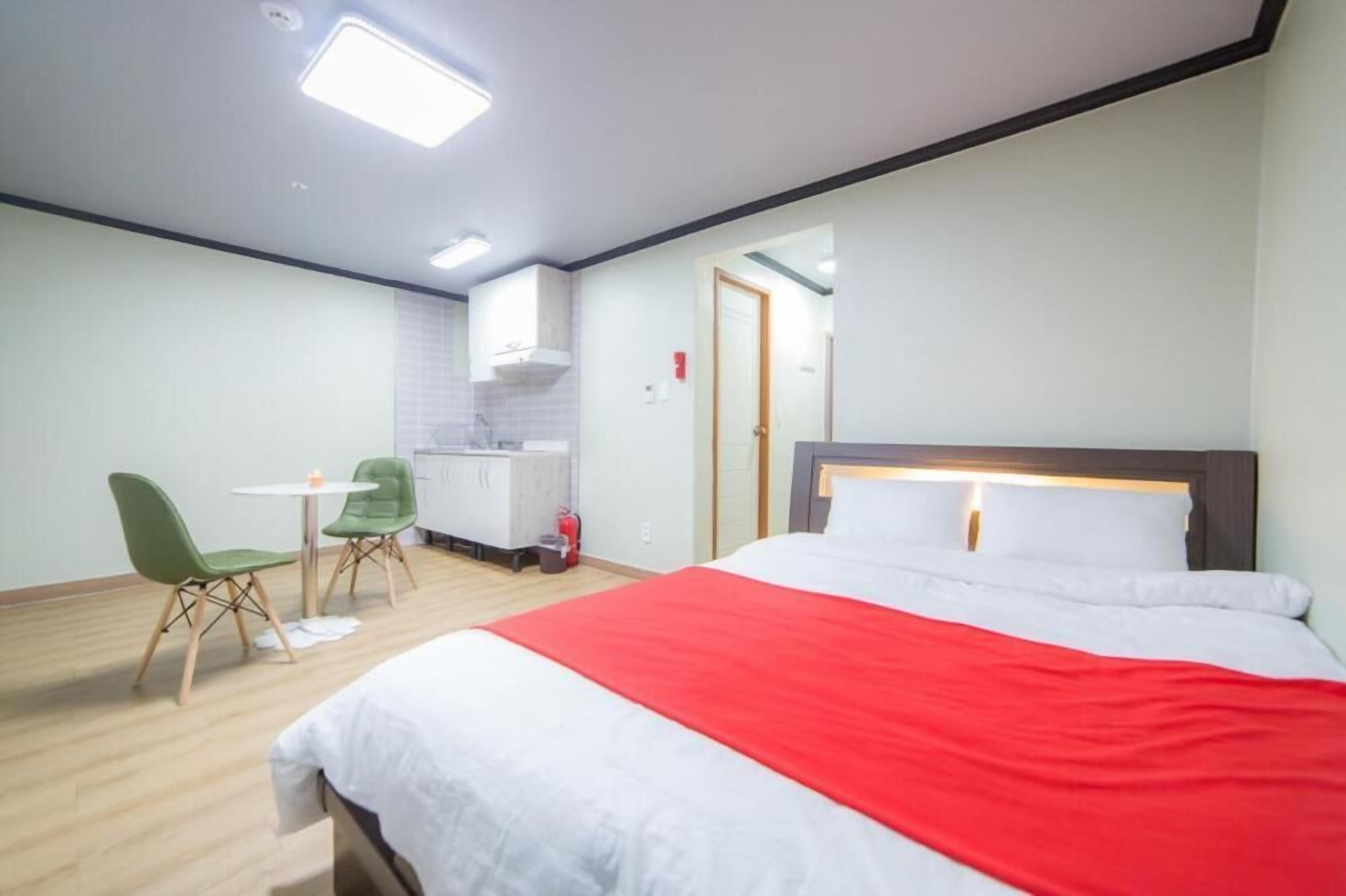 A hotel room with a bed, a desk, two chairs, a kitchenette, and a door.