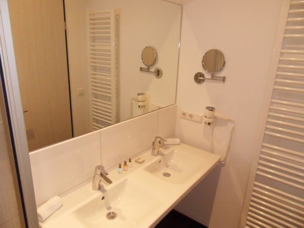 Un baño con un lavamanos blanco, dos espejos y un perchero para toallas.