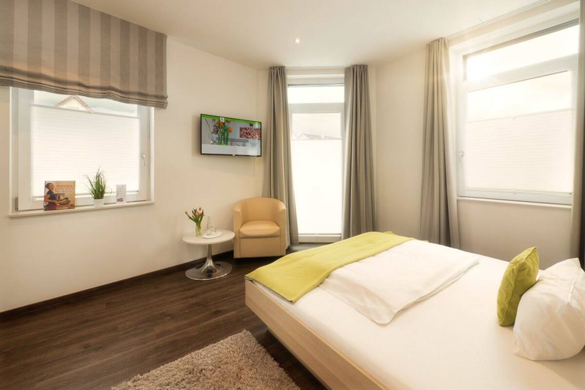 Une chambre d’hôtel moderne avec un grand lit, une petite table ronde, une chaise et un téléviseur fixé au mur.