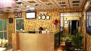 En reception med tapetseret væg, receptionistskranke, ure, et fjernsyn og potteplanter.