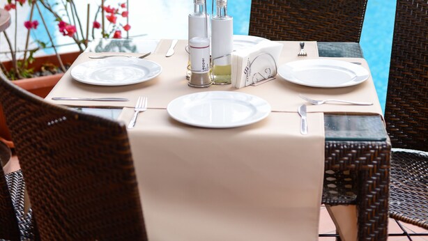A dining table set for two with plates, cutlery, and a bottle of water, overlooking a swimming pool. - Hotel Tarsis Club - All Inclusive (Sunny Beach)