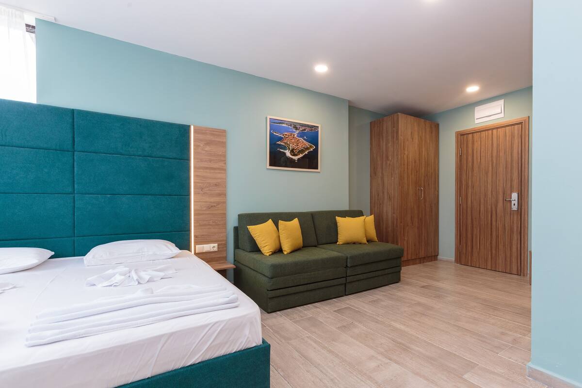 A modern bedroom with a bed, a green sofa with yellow cushions, and a wooden wardrobe.