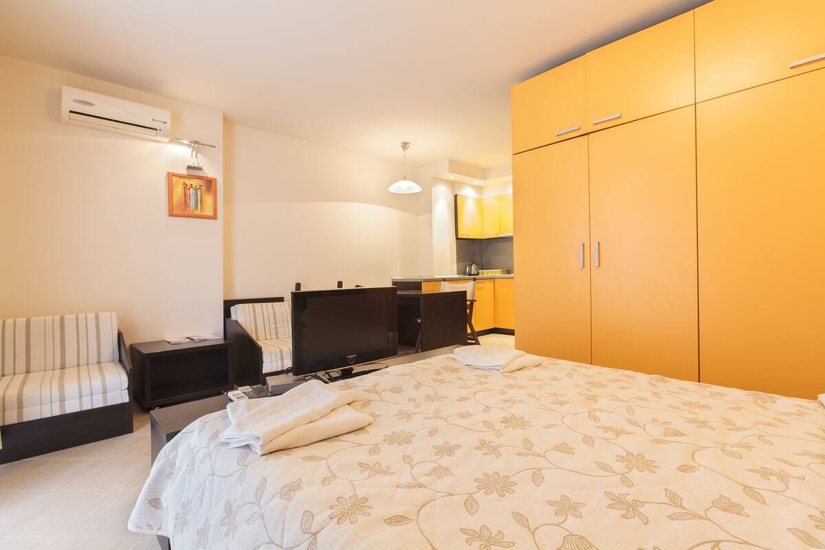 A hotel room with a bed, a TV, a desk, a chair, and a wardrobe.