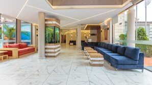 A spacious lobby with a long blue sofa, a red sofa, and a wooden bench area. - Hotel Tarsis Club - All Inclusive (Sunny Beach)