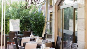 An outdoor dining area with wicker chairs and tables, a chandelier, and a view of greenery. - Hotel Tarsis Club - All Inclusive (Sunny Beach)