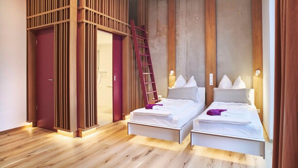 Un dormitorio moderno con dos camas, un separador de madera y una escalera.