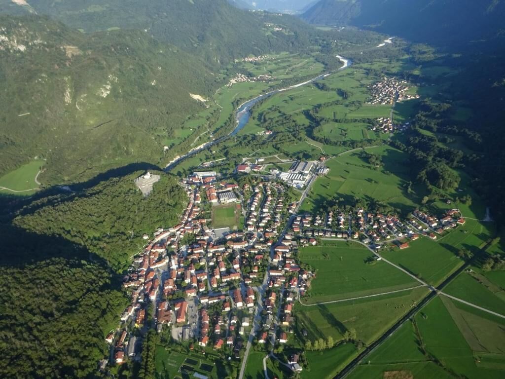Oversigtsbillede af en by med en flod, grønne marker og en blanding af boliger og erhvervsbygninger.