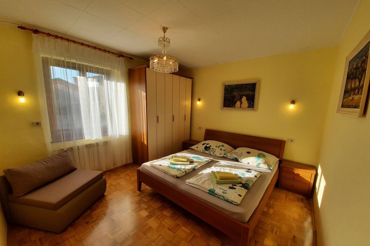 A bedroom with a bed, a sofa, a wardrobe, and a chandelier.