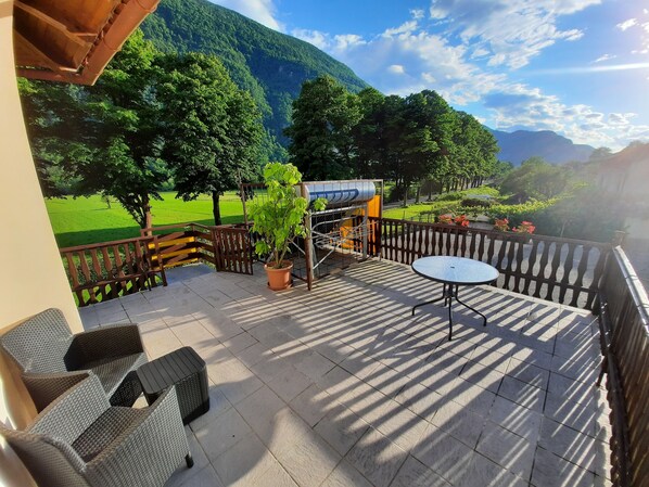 A terrace with wicker furniture, a potted plant, and a view of a green field and mountains. -  Apartment Zonir with sauna (Kobarid)