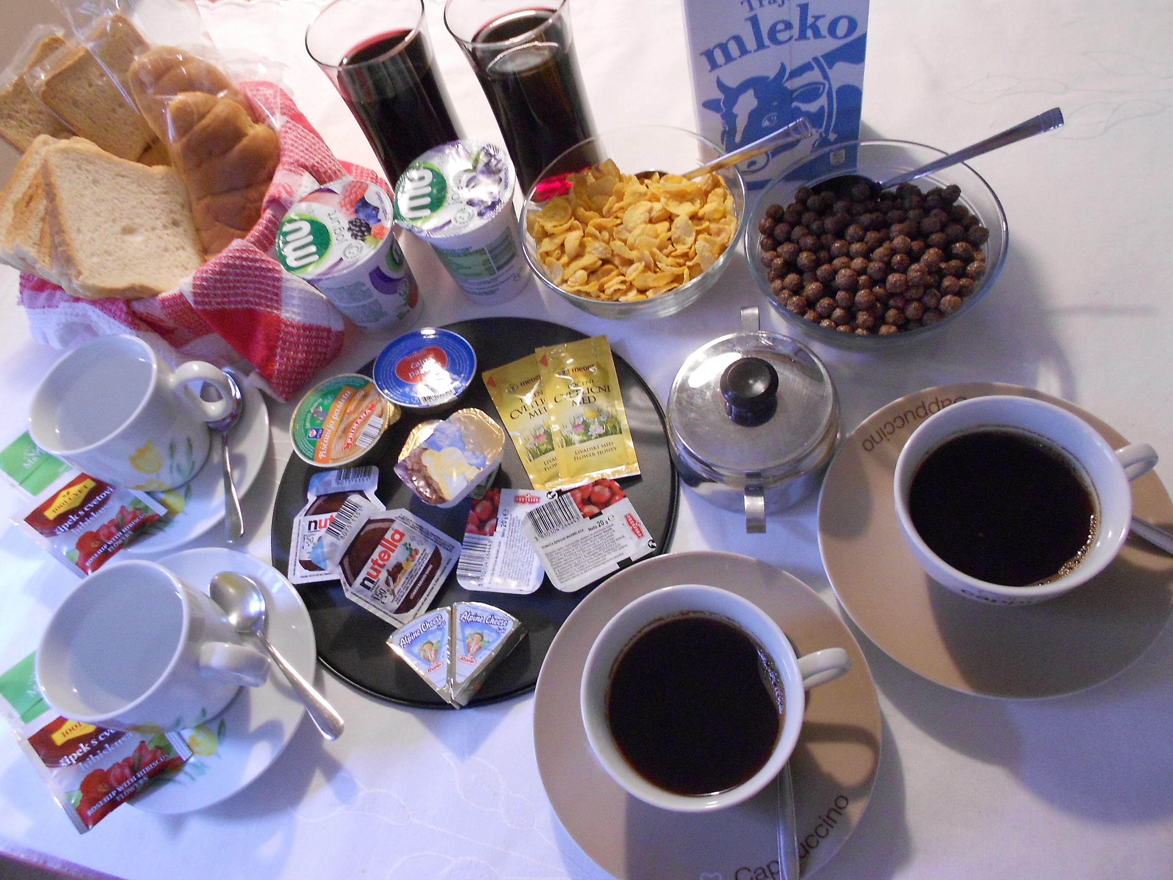 Una mesa de desayuno con diversos alimentos y bebidas, como pan, cereal, café y salsas.