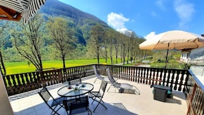 A balcony with a table and chairs, a view of a green field and trees, and a mountain in the background. -  Apartment Zonir with sauna (Kobarid)