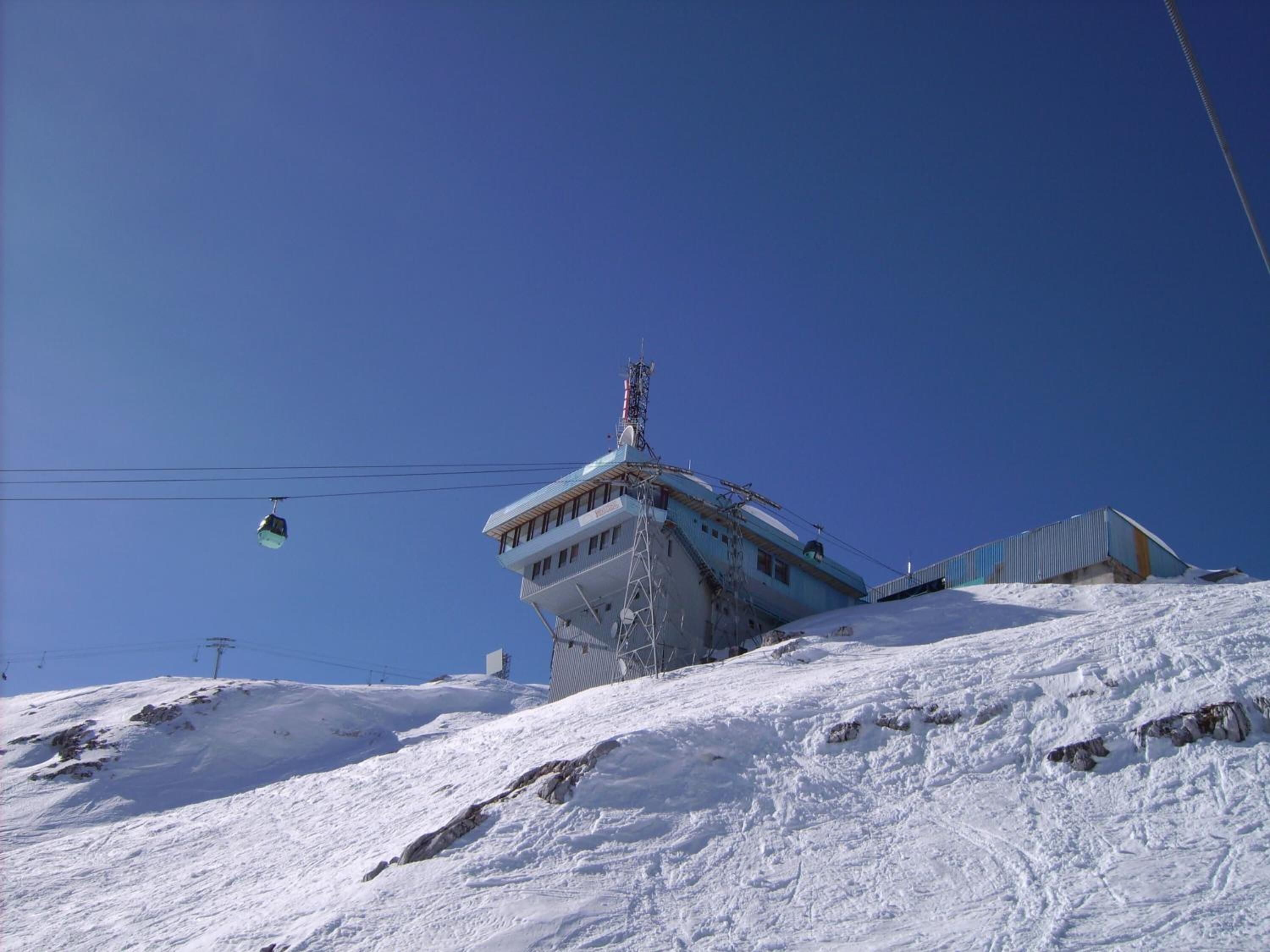 A snow-covered mountain with a ski lift and a building with a sloped roof.
