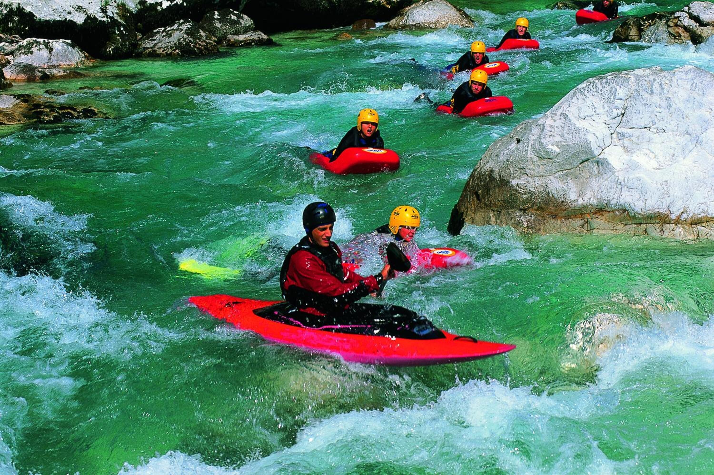 A group of people kayaking on a river with rocks and greenery in the background.