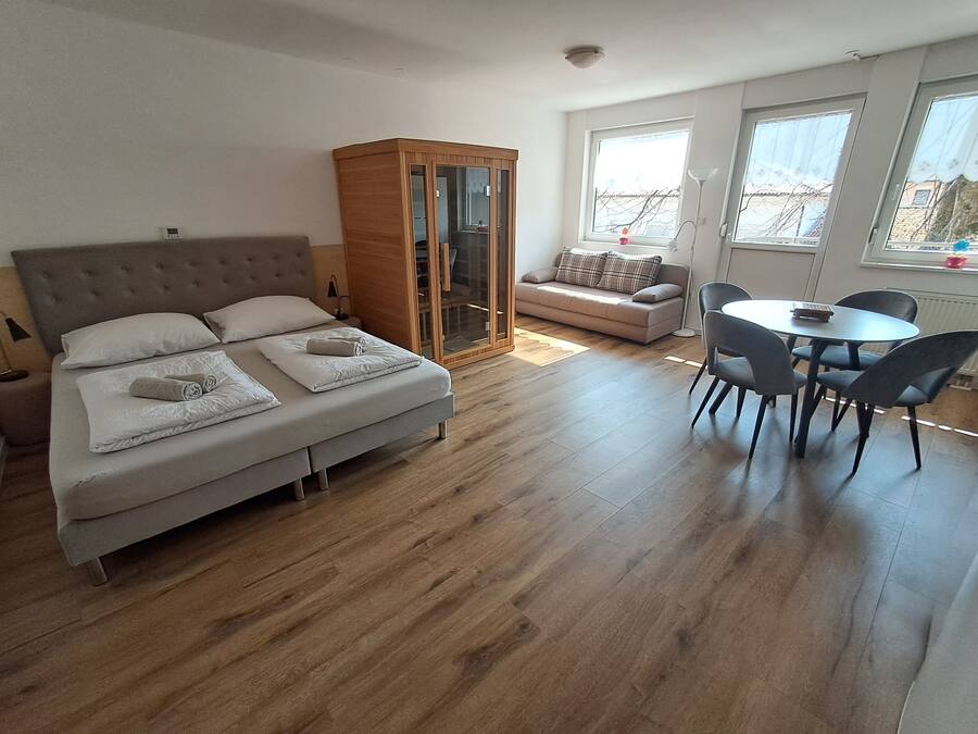 A modern bedroom with a bed, a wardrobe, a sofa, and a dining area.