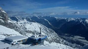 Montanha coberta de neve com uma estação de esqui, destacando um edifício com fachada de vidro e um teleférico em primeiro plano.