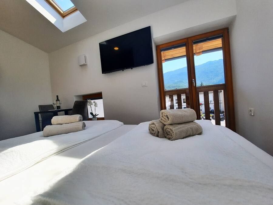 Habitación de hotel con dos camas, un televisor, un ventanal con vistas a montañas y una mesa con una botella y vasos.