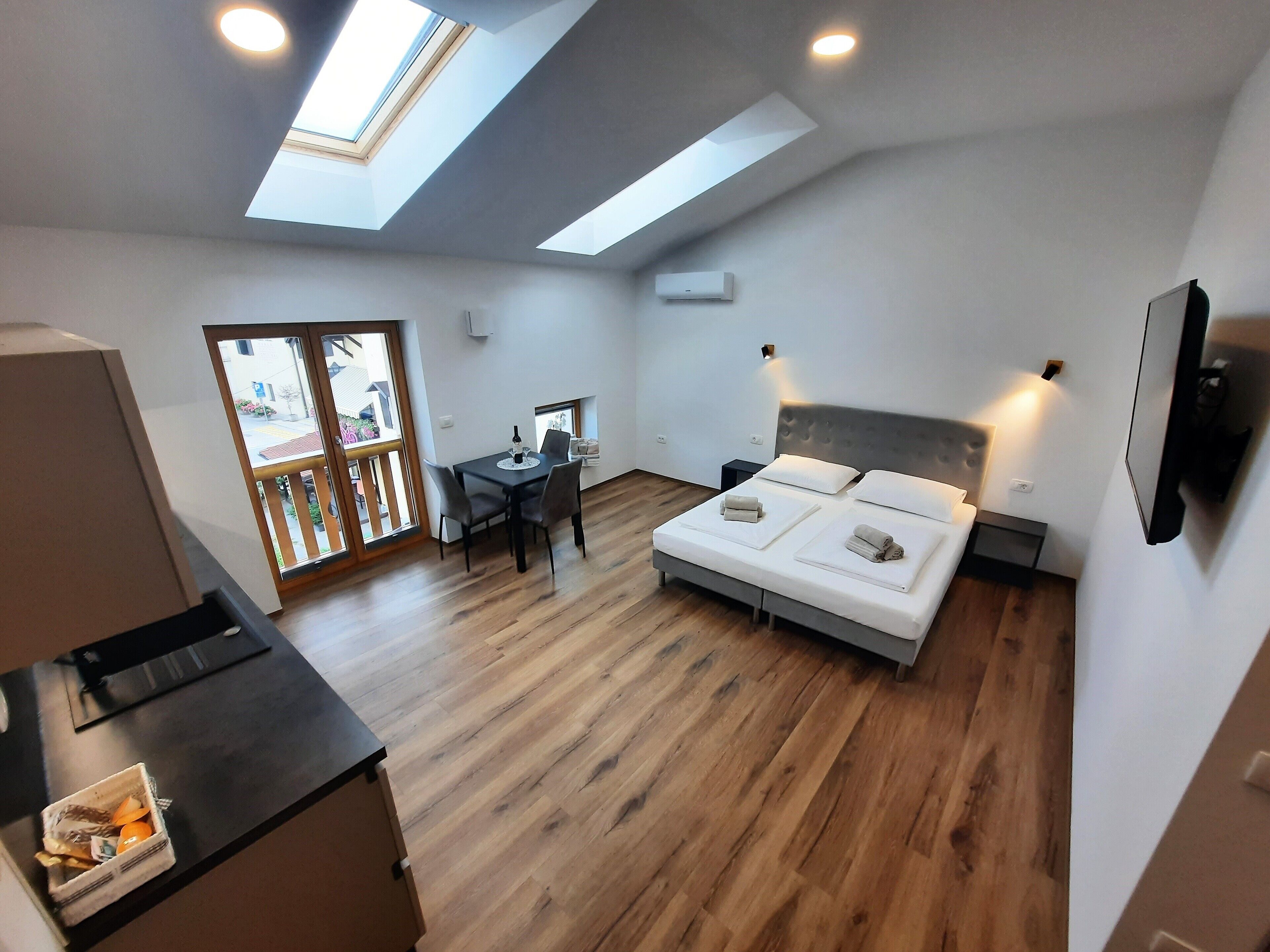 Un dormitorio moderno con tragaluz, una cama con almohadas, una mesita de noche y un pequeño escritorio con una silla.