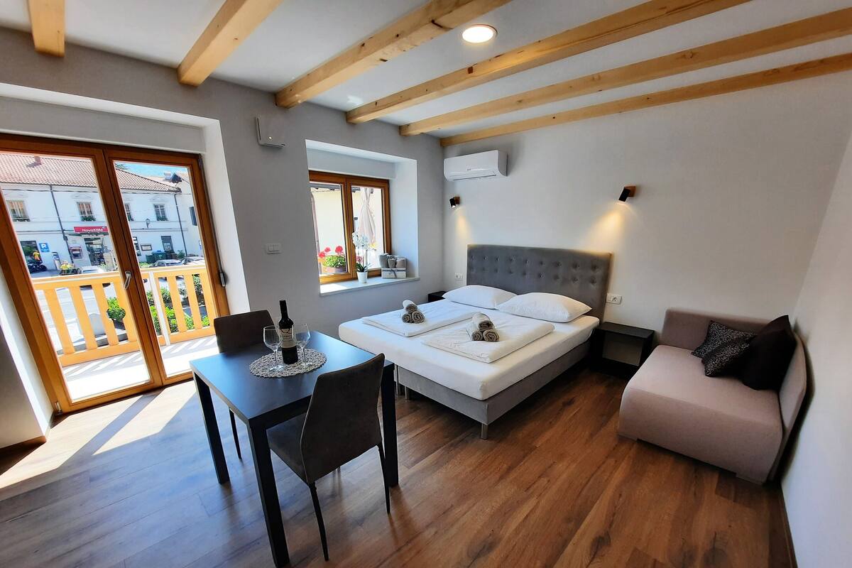 A bedroom with a bed, a bedside table, a window, and a balcony.