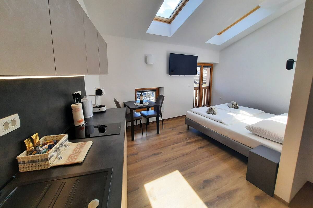 A compact room with a bed, a desk, a chair, a television, and a skylight.
