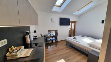 A compact room with a bed, a desk, a chair, a television, and a skylight.