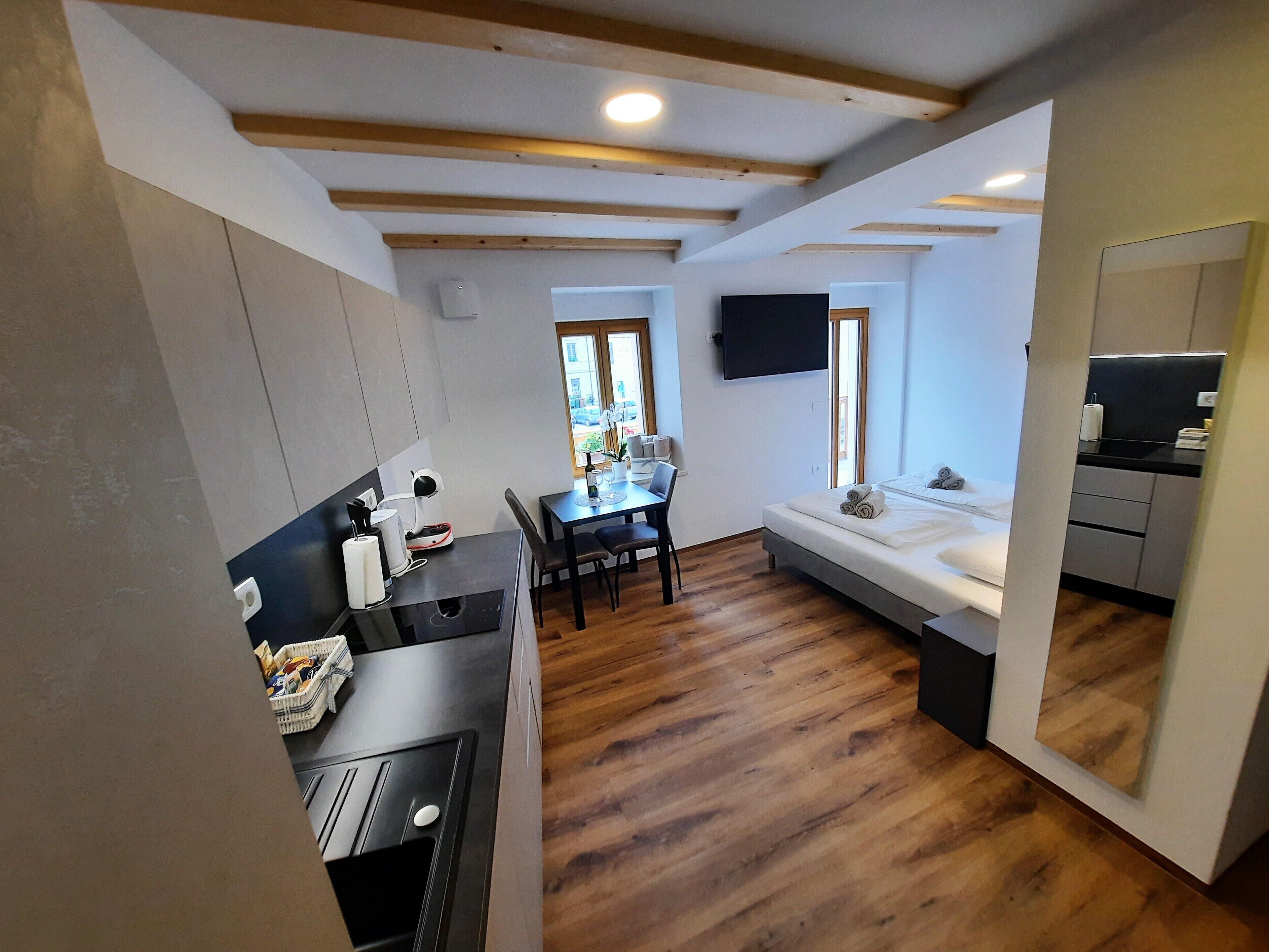 A compact hotel room with a kitchenette, a dining area, a bed, and a large mirror.