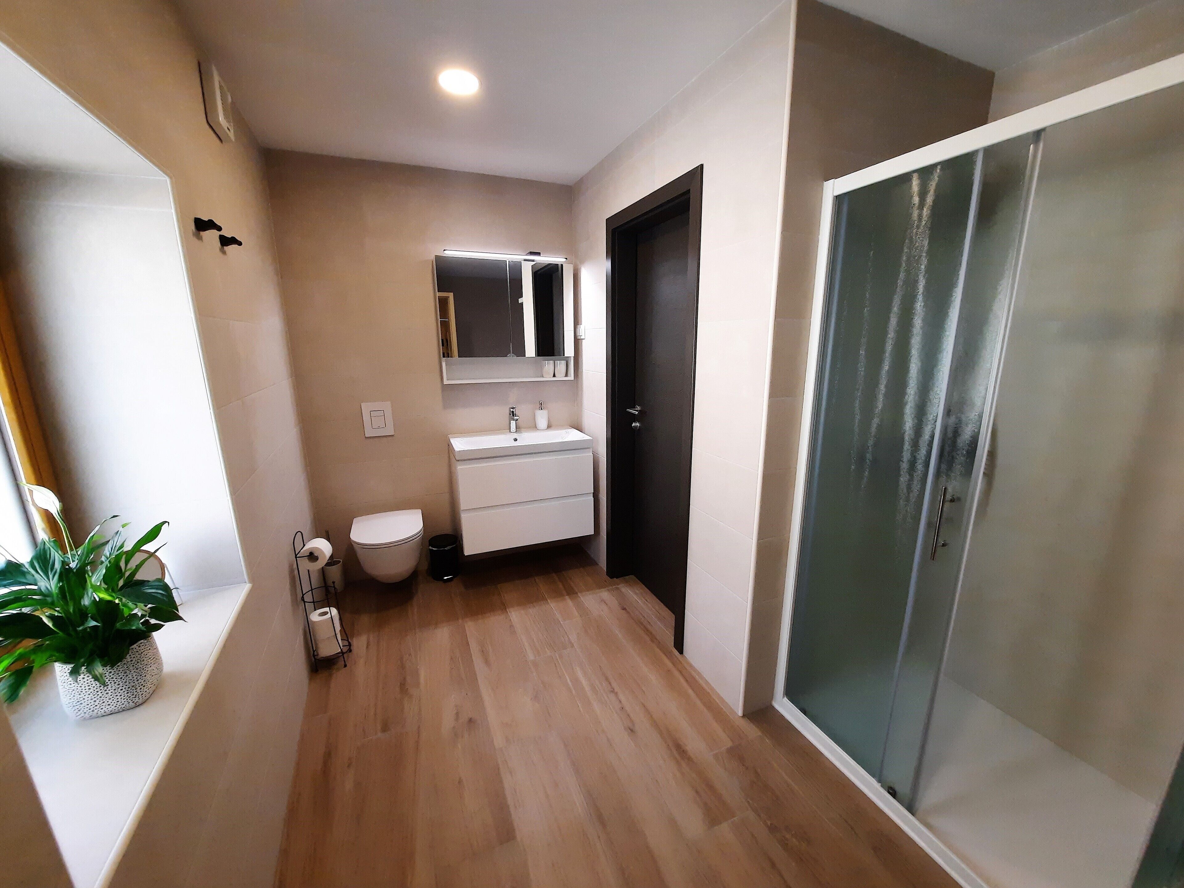 A modern bathroom with a wooden floor, white sink, and a glass shower enclosure.