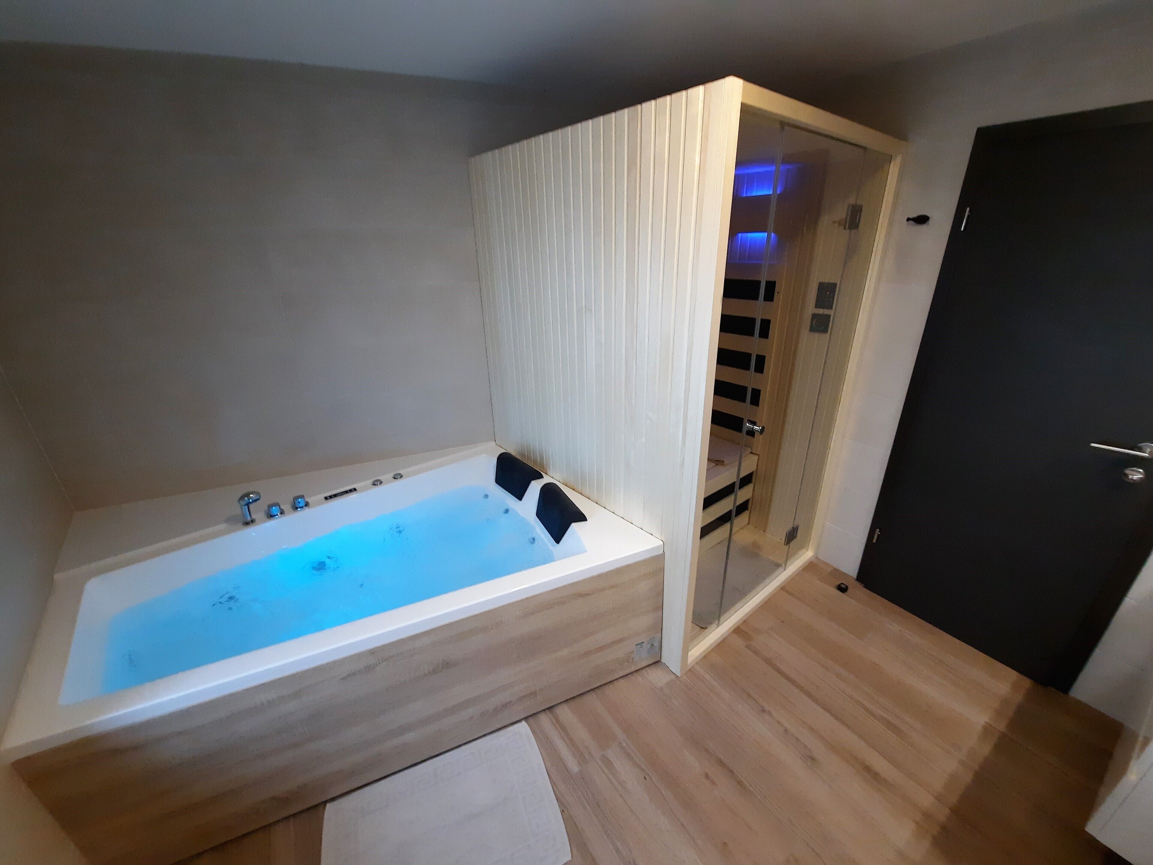 Ein modernes Badezimmer mit einer großen Badewanne, Holzboden und einer Tür zu einem Kleiderschrank.