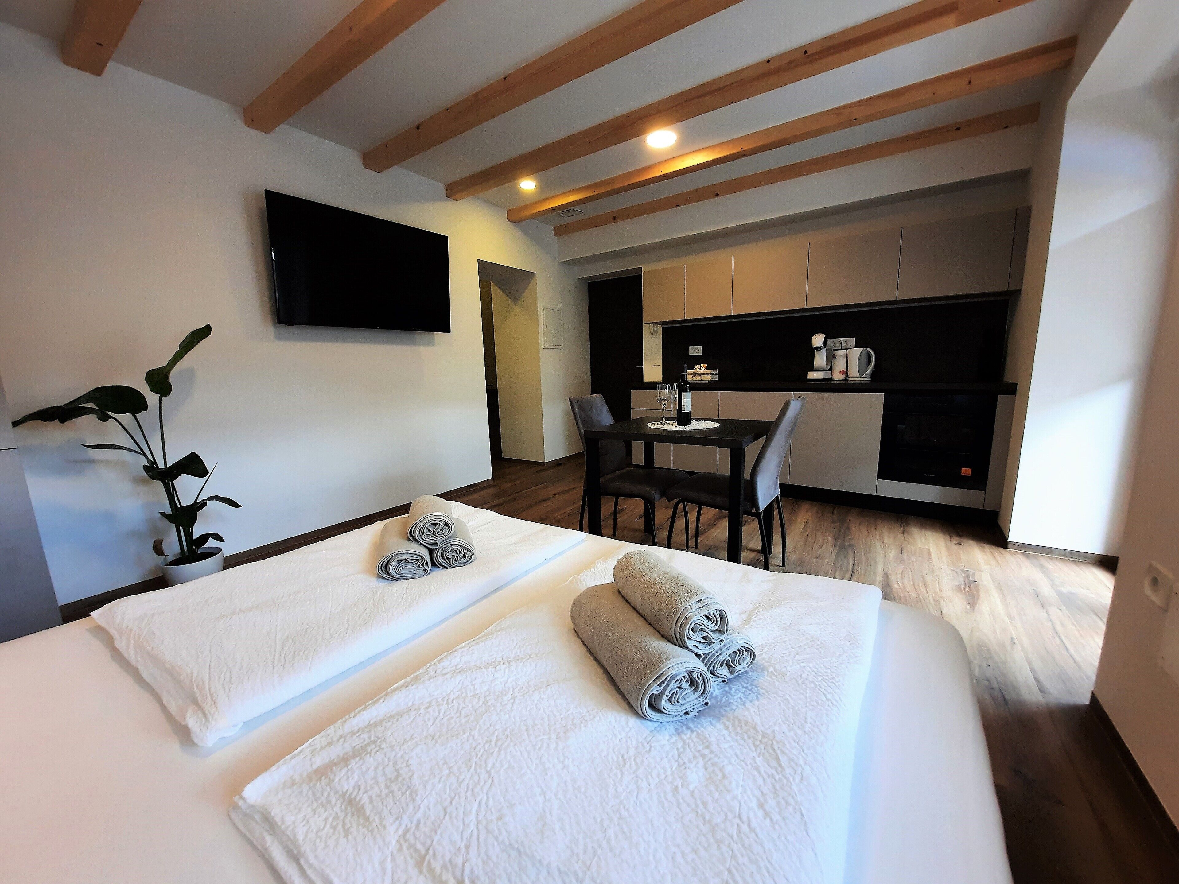 A modern hotel room with two beds, a dining area, and a TV on the wall.
