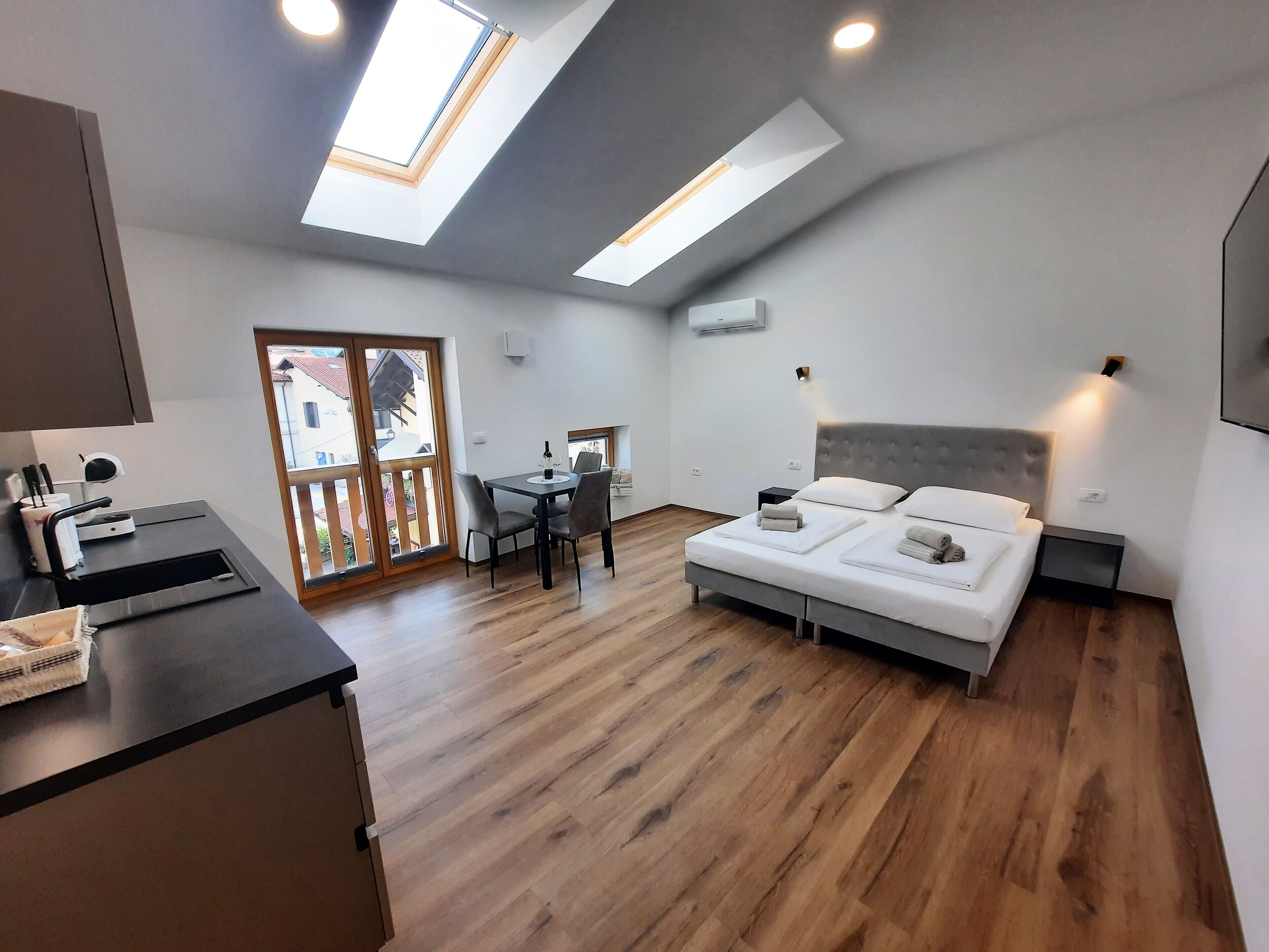 A modern bedroom with a large bed, a desk, and a dining table. There are skylights and a view of the outside.