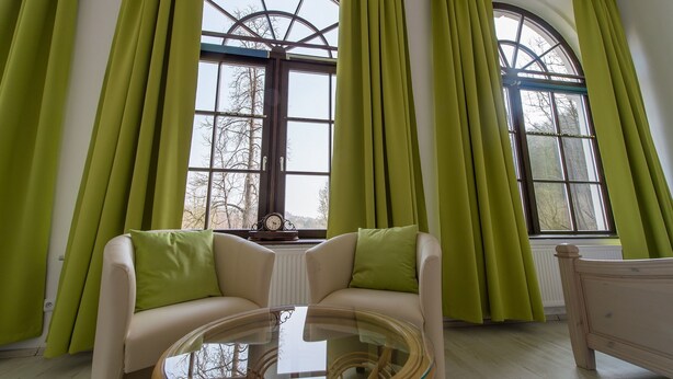 A room with a large arched window, a sofa with green cushions, and a glass coffee table.
