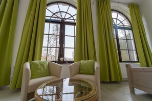 Ein Zimmer mit einem großen Bogenfenster, einem Sofa mit grünen Kissen und einem Glastisch.