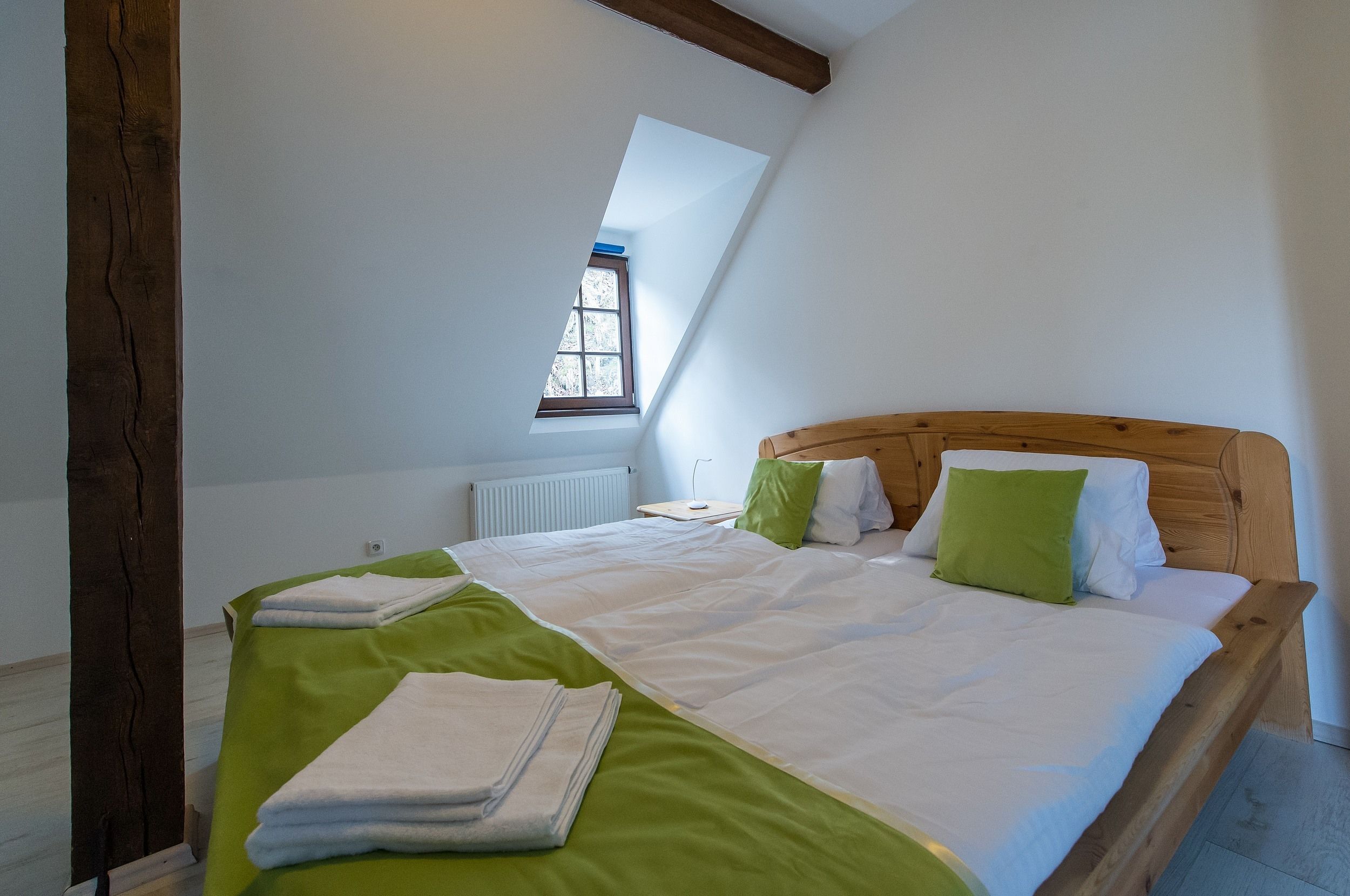 A bedroom with a sloped ceiling, a wooden headboard, a large bed with green and white bedding, and a small window.