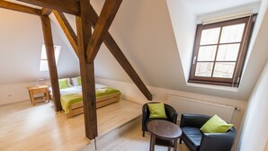 A room with a loft bed, a small table, a sofa, and a window with a view.