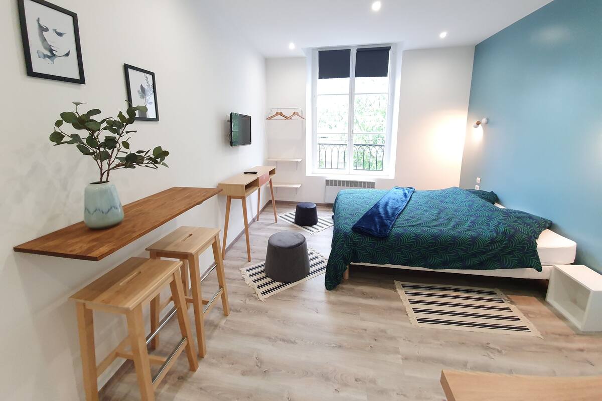 Quarto moderno com cama, escrivaninha, cadeira, planta em vaso e janela.