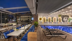 Eine Dachterrasse mit Pool, Sitzbereichen und einer Bar mit Blick auf die Stadt.