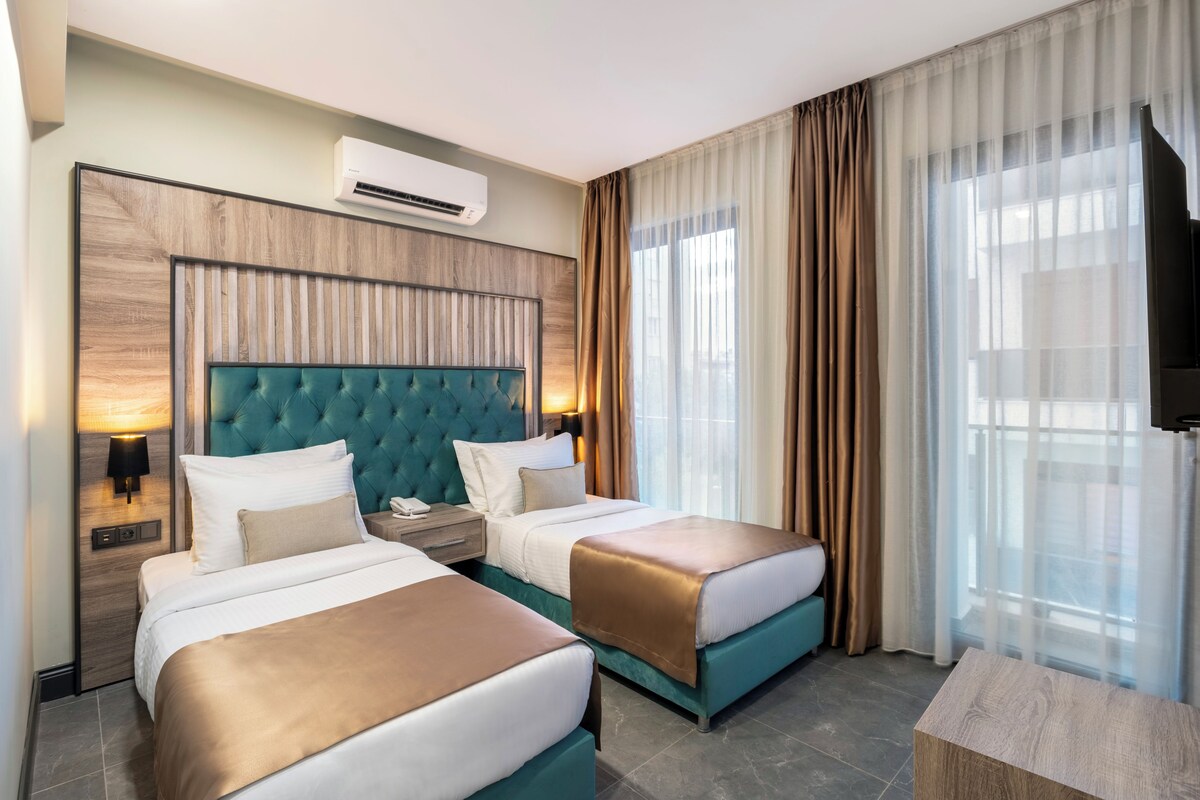 A hotel room with two beds, a large headboard, an air conditioning unit, a TV, and a window with curtains.