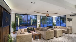 Eine großzügige Lobby mit mehreren Sitzbereichen, großen Fenstern mit Blick ins Freie und einem modernen Deckenstil.