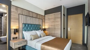 Ein modernes Hotelzimmer mit einem großen Bett, einem Holzkopfteil, einem Nachttisch, einem Kleiderschrank und einem Fernseher.