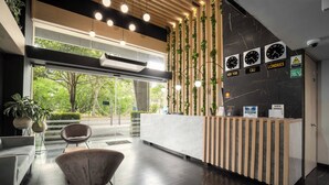A modern reception area with a marble reception desk, a wooden reception stand, and a seating area with a chair. - Hotel Plaza Del Lili (Cali)