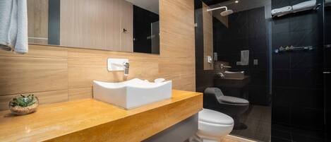 Un baño moderno con tocador de madera, lavamanos blanco, inodoro y cabina de ducha con mampara de vidrio.