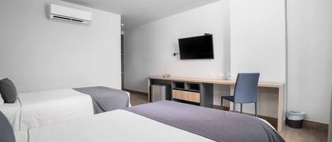 Habitación de hotel moderna con dos camas, un escritorio, una silla y un televisor de pantalla plana montado en la pared.