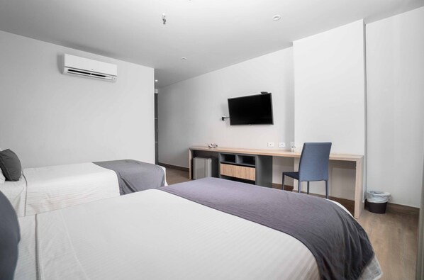 A modern hotel room with two beds, a desk, a chair, and a flat-screen TV mounted on the wall.