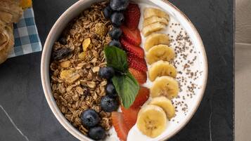 Een kom met granola, aardbeien, bananen en blauwe bessen op een donkere ondergrond.
