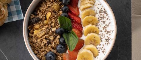 Un tazón de granola con fresas, plátanos y arándanos sobre una superficie oscura.