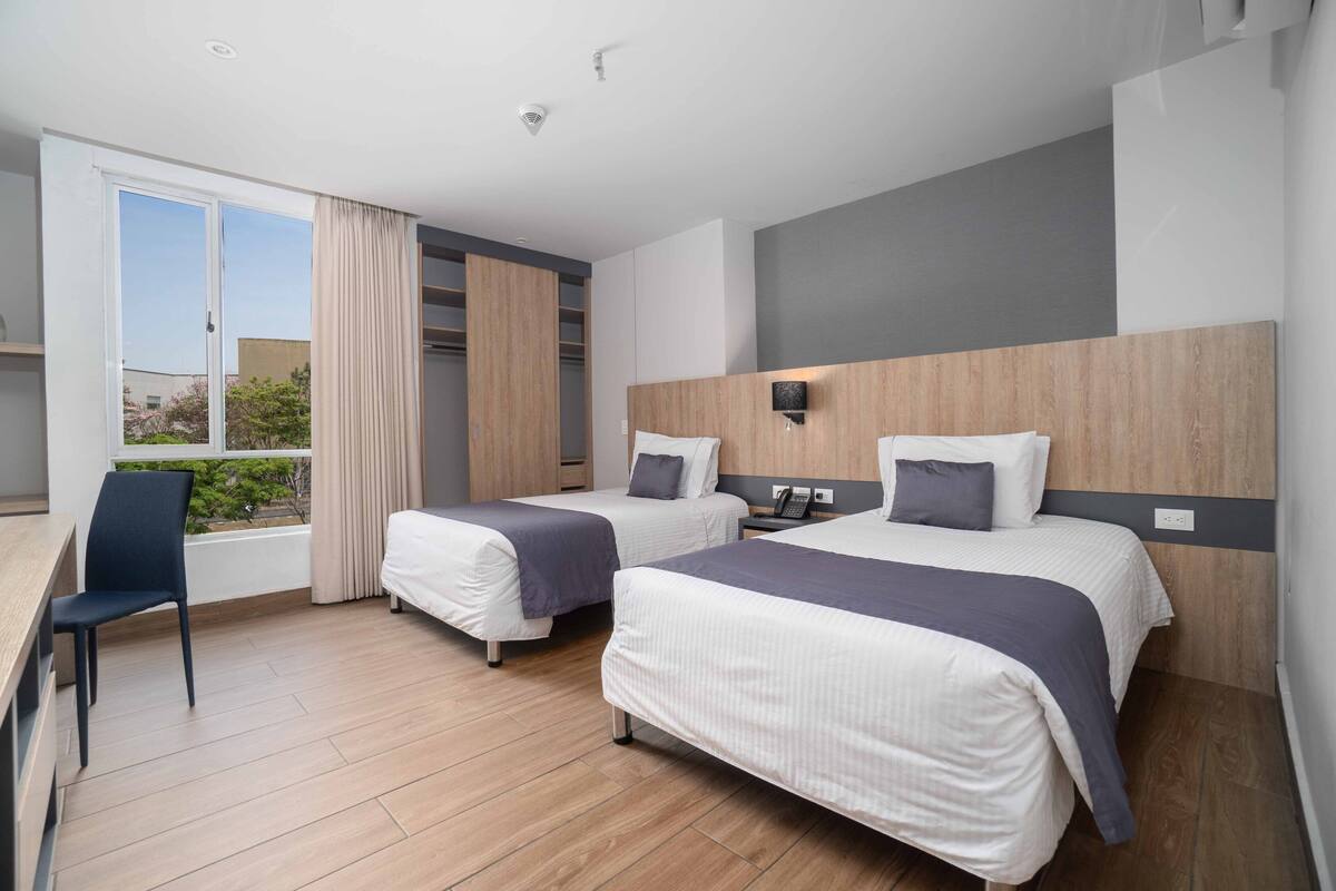 A modern hotel room with two beds, a desk, and a chair.